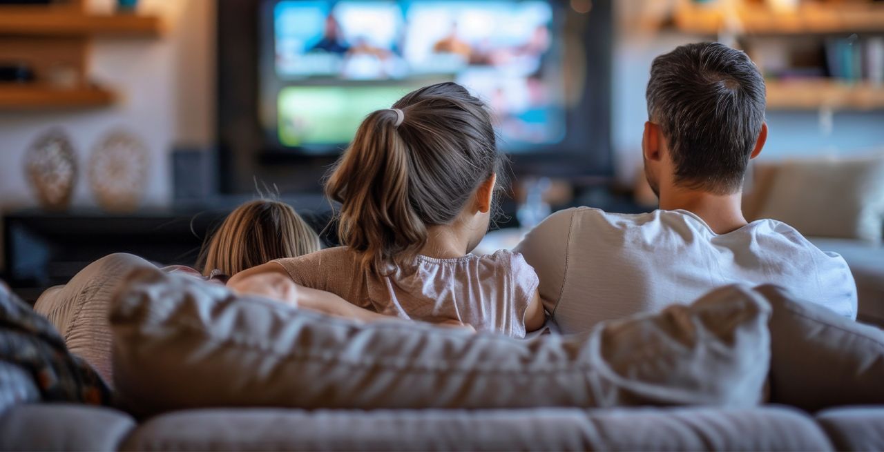 Family watching TV programming from their living room couch, viewed from behind