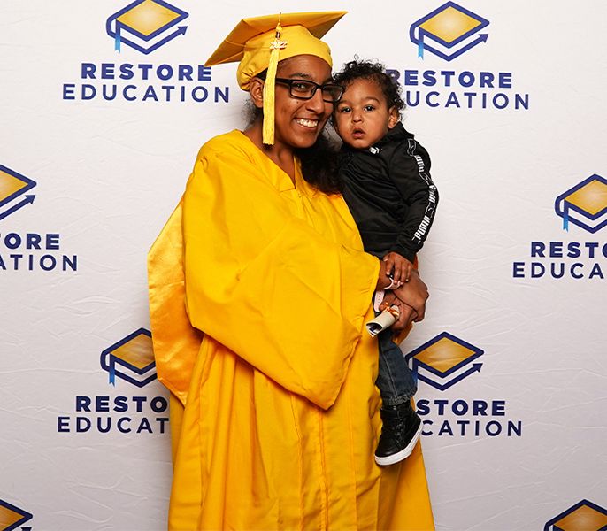 Restore Education student Miquella poses with her child at her graduation