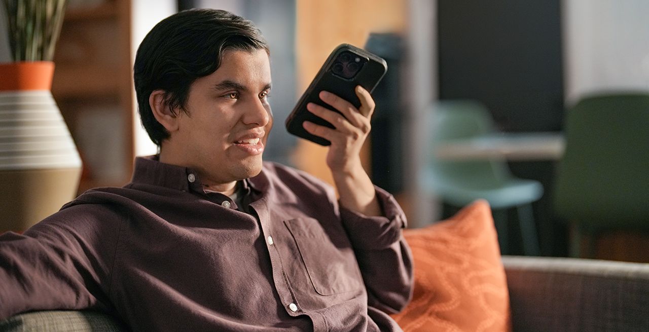 Sight impaired man using his cell phone for audio while watching TV at home