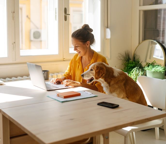 Woman working on her laptop at home with her dog by her side 